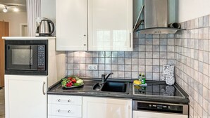 Eine moderne Küche mit weißen Schränken, einer eingebauten Mikrowelle, einer Edelstahl-Dunstabzugshaube und einer gefliesten Spritzschutzwand.