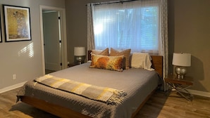 Un dormitorio con cama, ventilador de techo, ventana con cortinas traslúcidas y dos lámparas de noche.