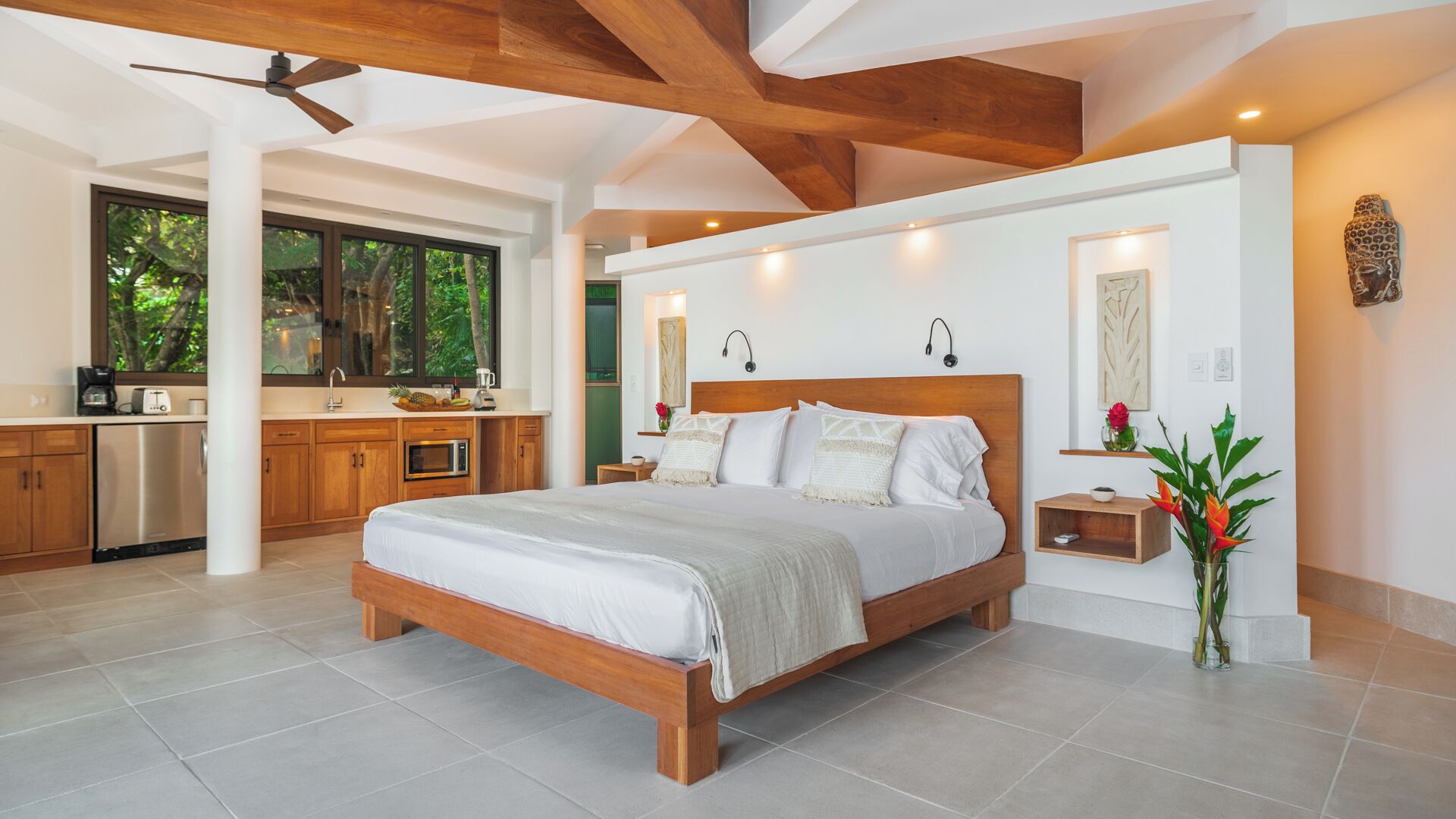 Une chambre à coucher moderne avec un lit en bois, un coin cuisine doté de meubles en bois et une grande fenêtre.