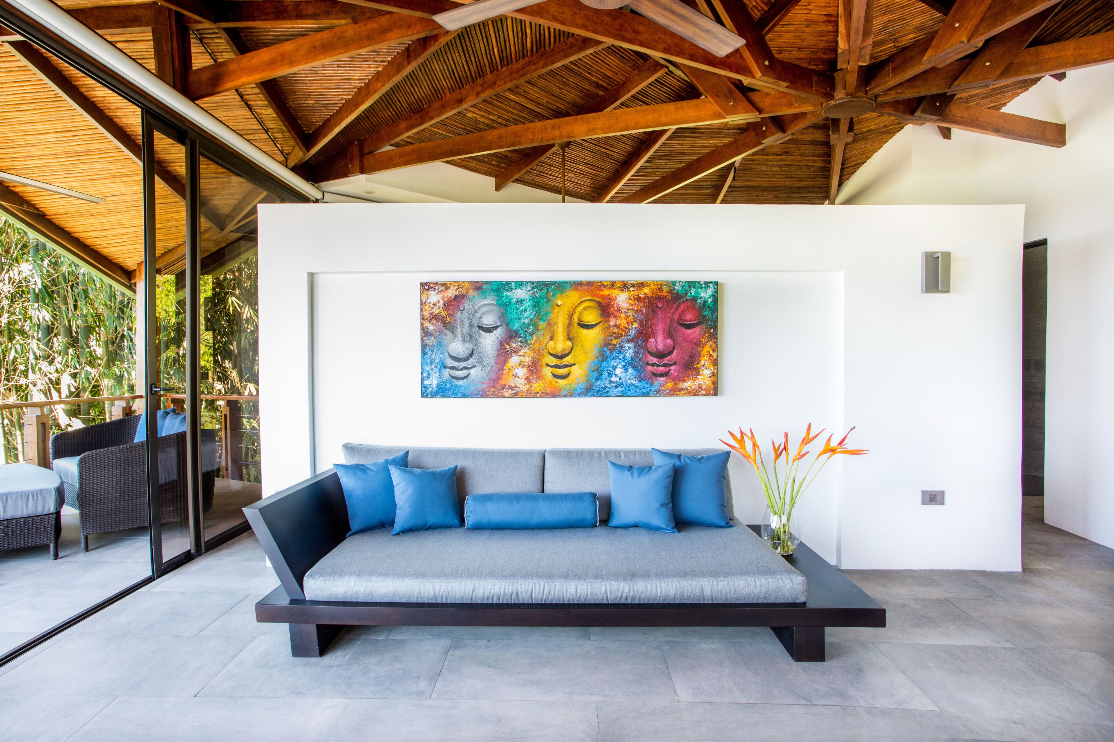 A modern living room with a sofa, a colorful abstract painting, and a vase with flowers.