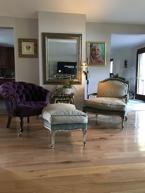 Un salón con un espejo grande, dos sillones, una mesita con una lámpara y un televisor.