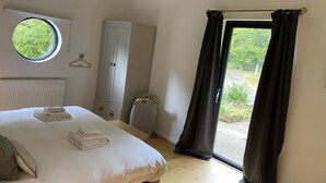 Un dormitorio con cama, armario, radiador, ventana con vistas a zonas verdes y puerta con cortinas.