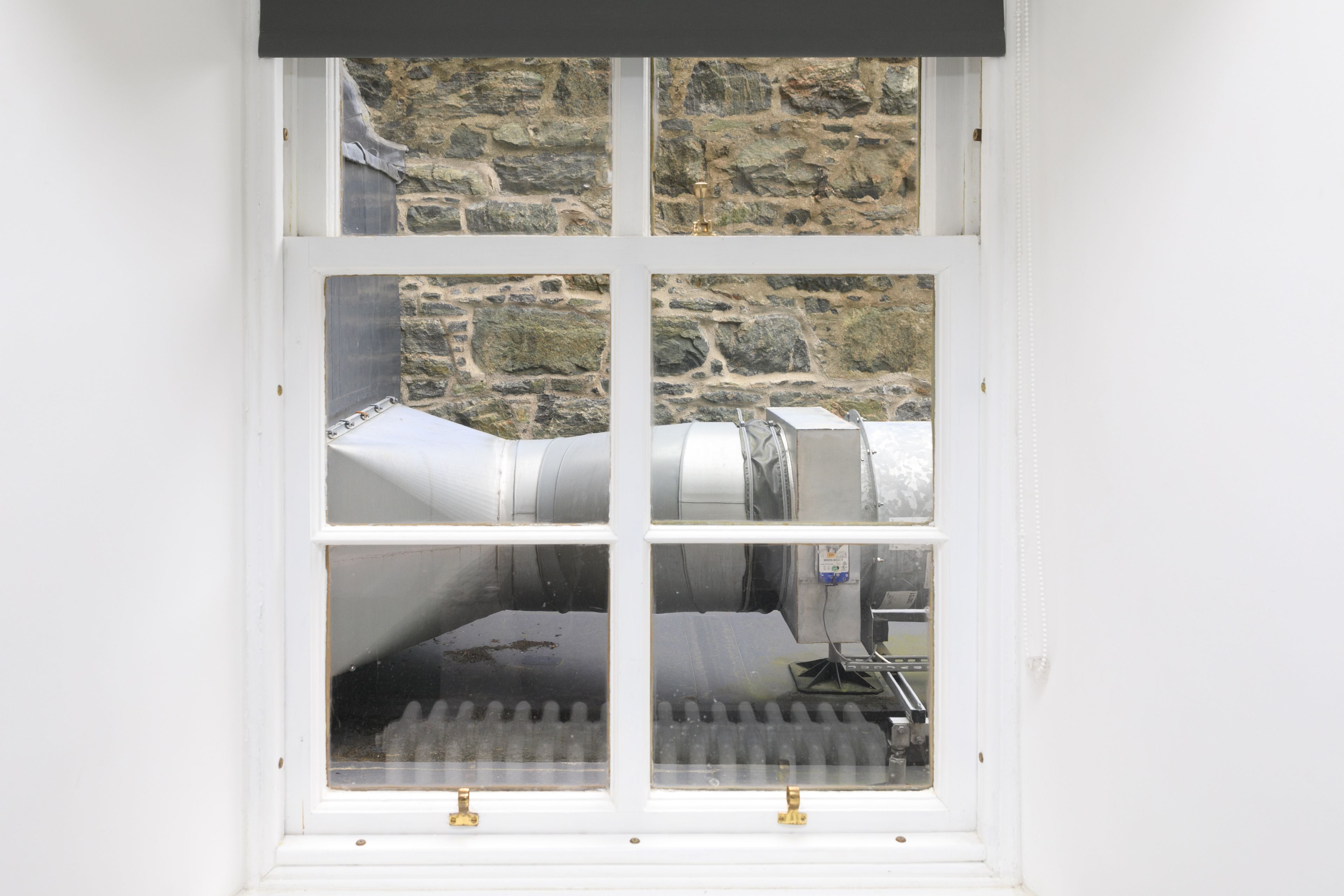 A window with a view of a stone wall and industrial equipment.