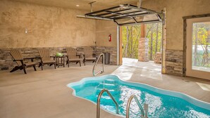 En indendørs swimmingpool med glasafskærmning, træstole og en stenvæg.