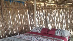 Una cama con colcha de rayas rojas y blancas, estructura de madera y techo de paja.