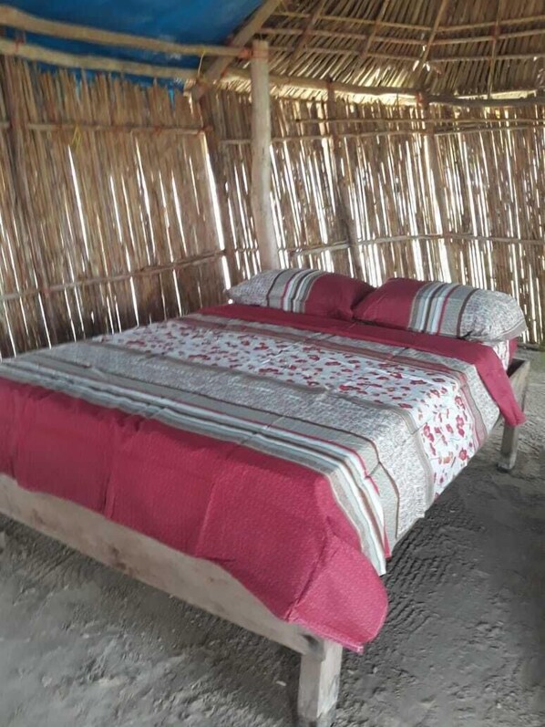 A bed with a red and white patterned bedspread, a wooden frame, and a straw ceiling. - Discovery Gunayar (Narganá)