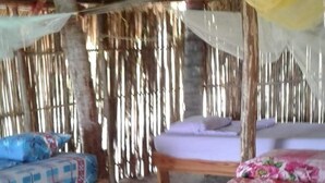 Una habitación rústica con techo de paja, una cama con colcha estampada de flores y un banco con cojín de diseño azulado.