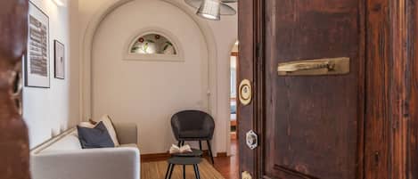 A hallway with a wooden door, a sofa, a chair, and a small table with a book.
