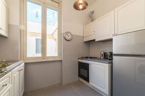 Eine Küche mit weißen Schränken, einem Herd, einem Kühlschrank und einer Wanduhr.