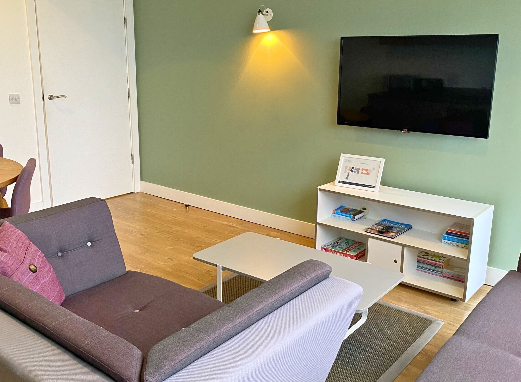 Een woonkamer met een bank, een salontafel, een boekenkast en een flatscreen televisie aan de muur.
