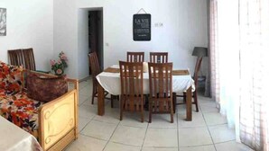 Ein Essbereich mit Tisch und Stühlen, ein Bett mit floralem Überwurf und ein Schild an der Wand.
