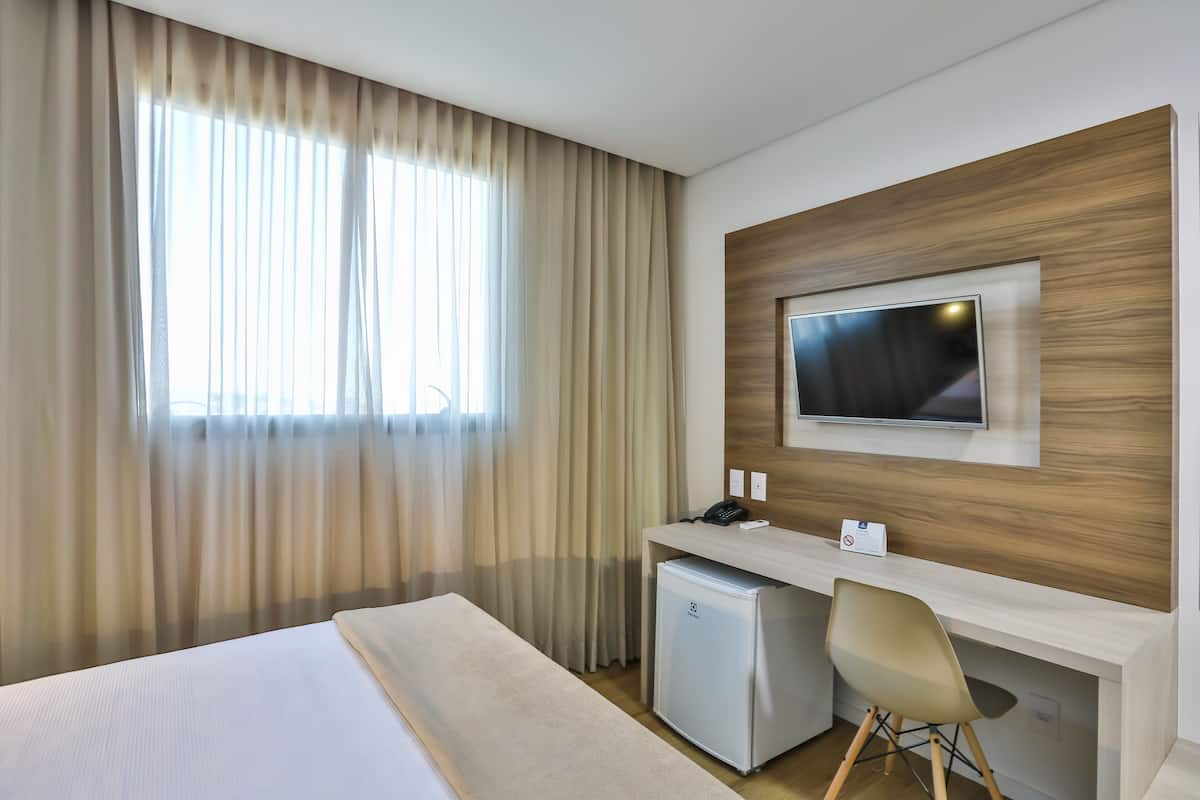 Ein Hotelzimmer mit Bett, Schreibtisch, Fernseher und kleinem Kühlschrank.