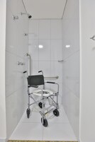Un box de ducha accesible en silla de ruedas, con ducha de mano, barras de apoyo y suelo antideslizante.