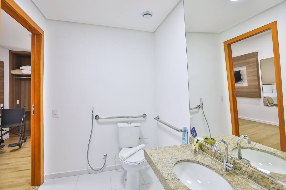 Ein modernes Badezimmer mit Toilette, Haltegriffen, Waschbecken und Spiegel.