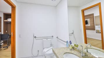 A modern bathroom with a toilet, grab bars, a sink, and a mirror.