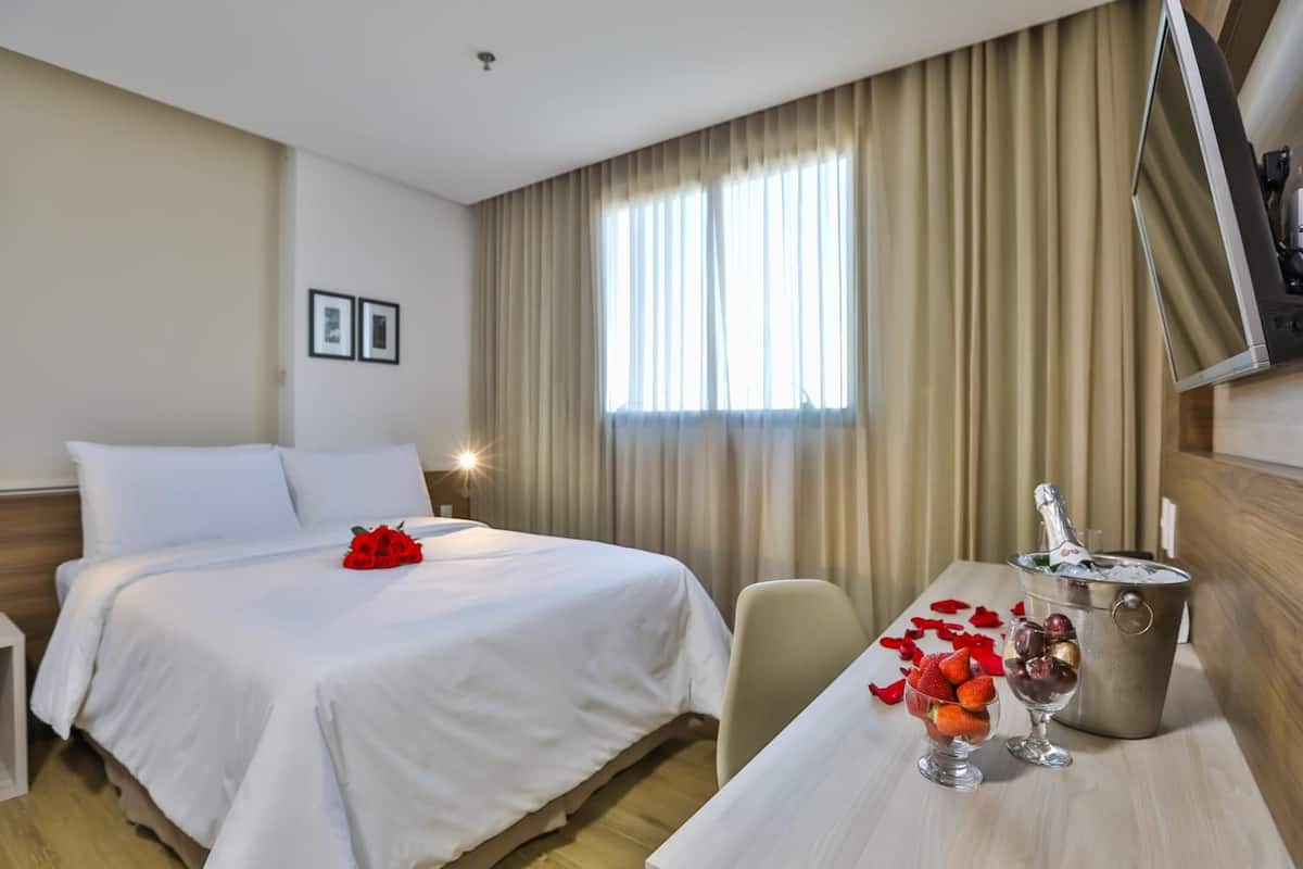 Ein Hotelzimmer mit Bett, Schreibtisch und Champagnerkühlbox sowie einem Fernseher an der Wand.