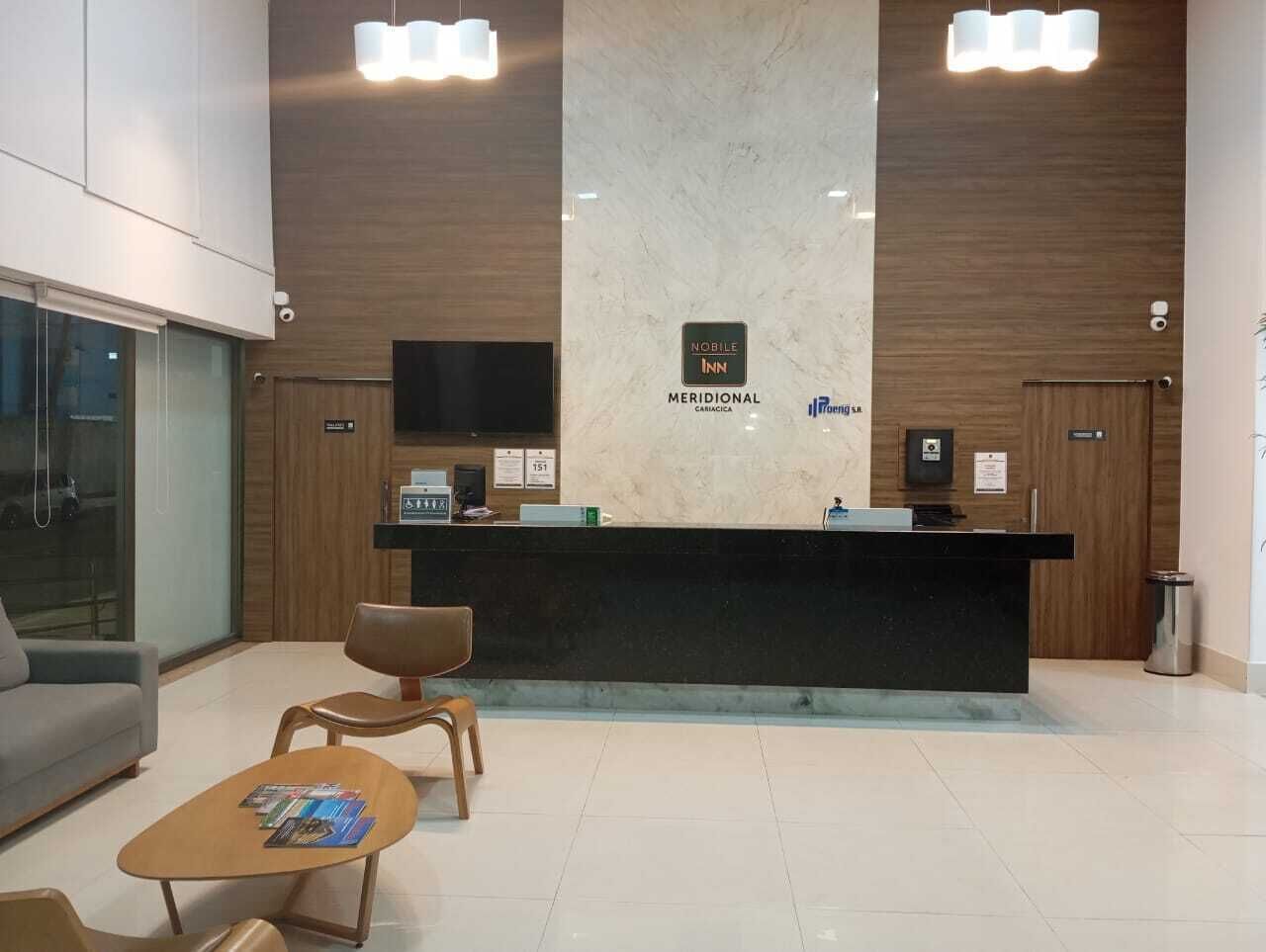 A hotel reception area with a marble reception desk, a sofa, and two wooden chairs.