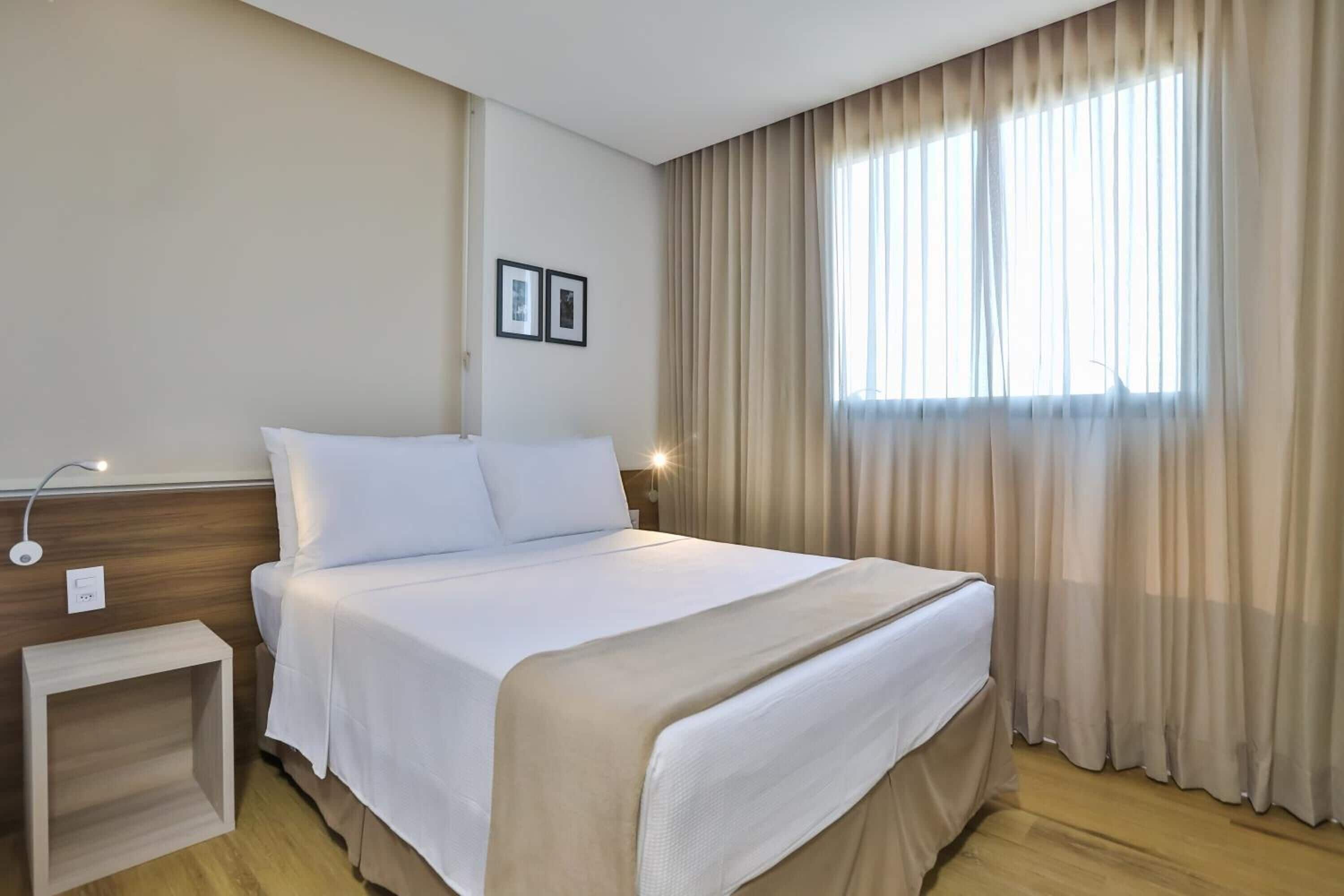 Habitación de hotel con cama, mesita de noche y ventana con cortinas.