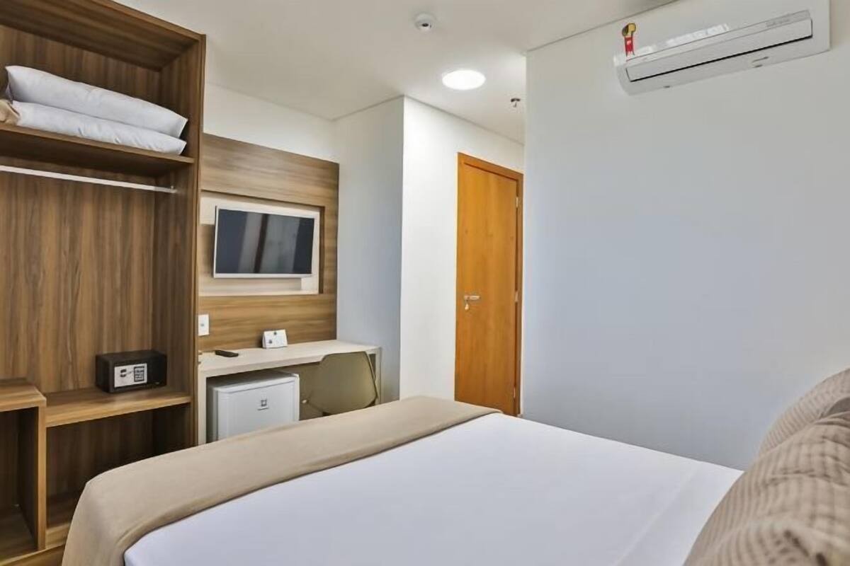 A hotel room with a bed, a desk with a computer, a TV, a wardrobe, and a door.