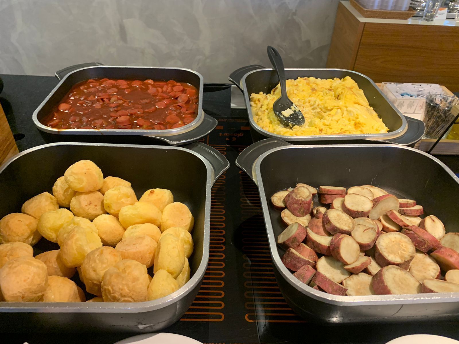 A buffet with various dishes including beans, scrambled eggs, bread rolls, and sliced sweet potatoes.