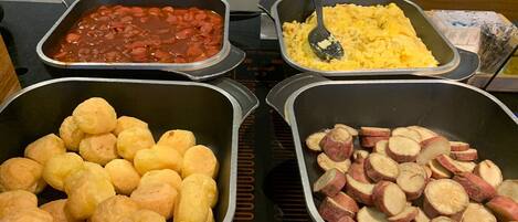 A buffet with various dishes including beans, scrambled eggs, bread rolls, and sliced sweet potatoes.