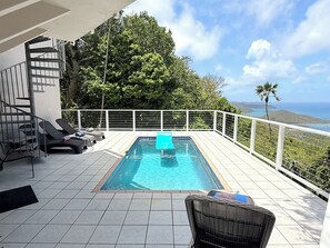 A swimming pool with lounge chairs and a view of the ocean.