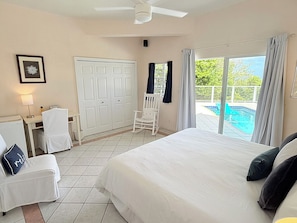 A bedroom with a large bed, a chair, a desk, and a view of a swimming pool.