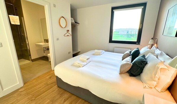 A bedroom with a bed, pillows, a window, a bathroom, and a towel rack.