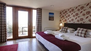 A hotel room with a bed, a view through a sliding glass door to an outdoor area, a radiator, and a floral-patterned wall. - Stables 2 -  a llyn peninsula that sleeps 2 guests  in 1 bedroom (Pwllheli)