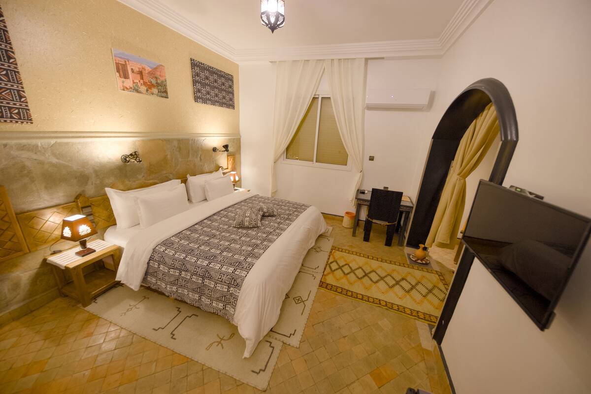 A hotel room with a bed, nightstand, lamp, and a TV mounted on the wall.