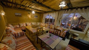 A cozy, well-lit room with striped sofas, a dining table, and a view of the outside. - Tin Joseph (Ouarzazate)