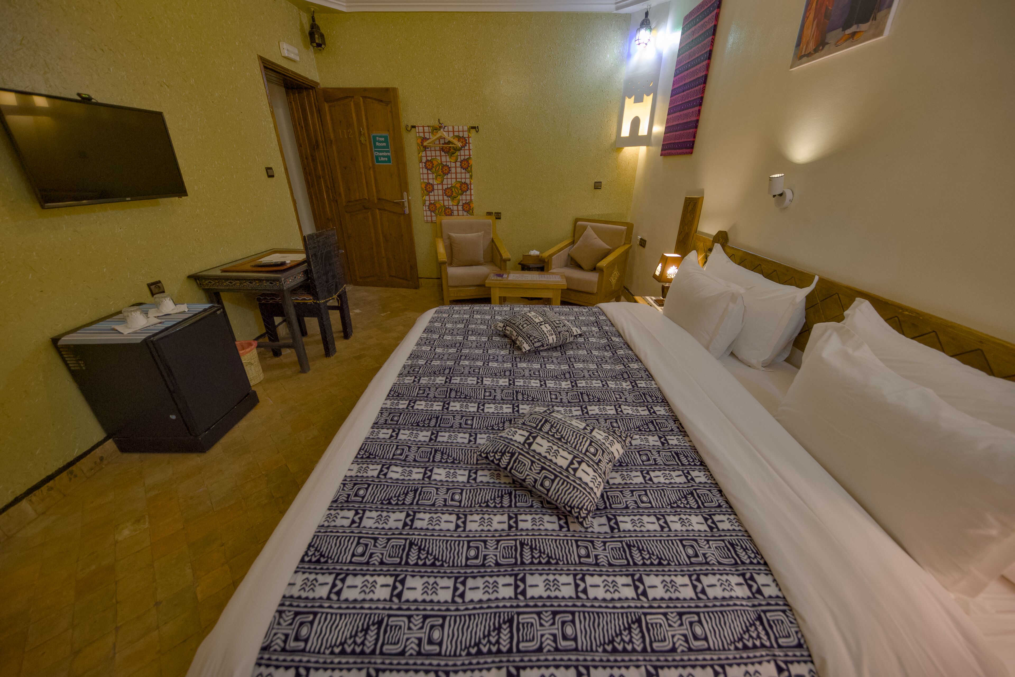 Una habitación de hotel con una cama grande, dos sillones, una mesita, un televisor y un escritorio con computadora.