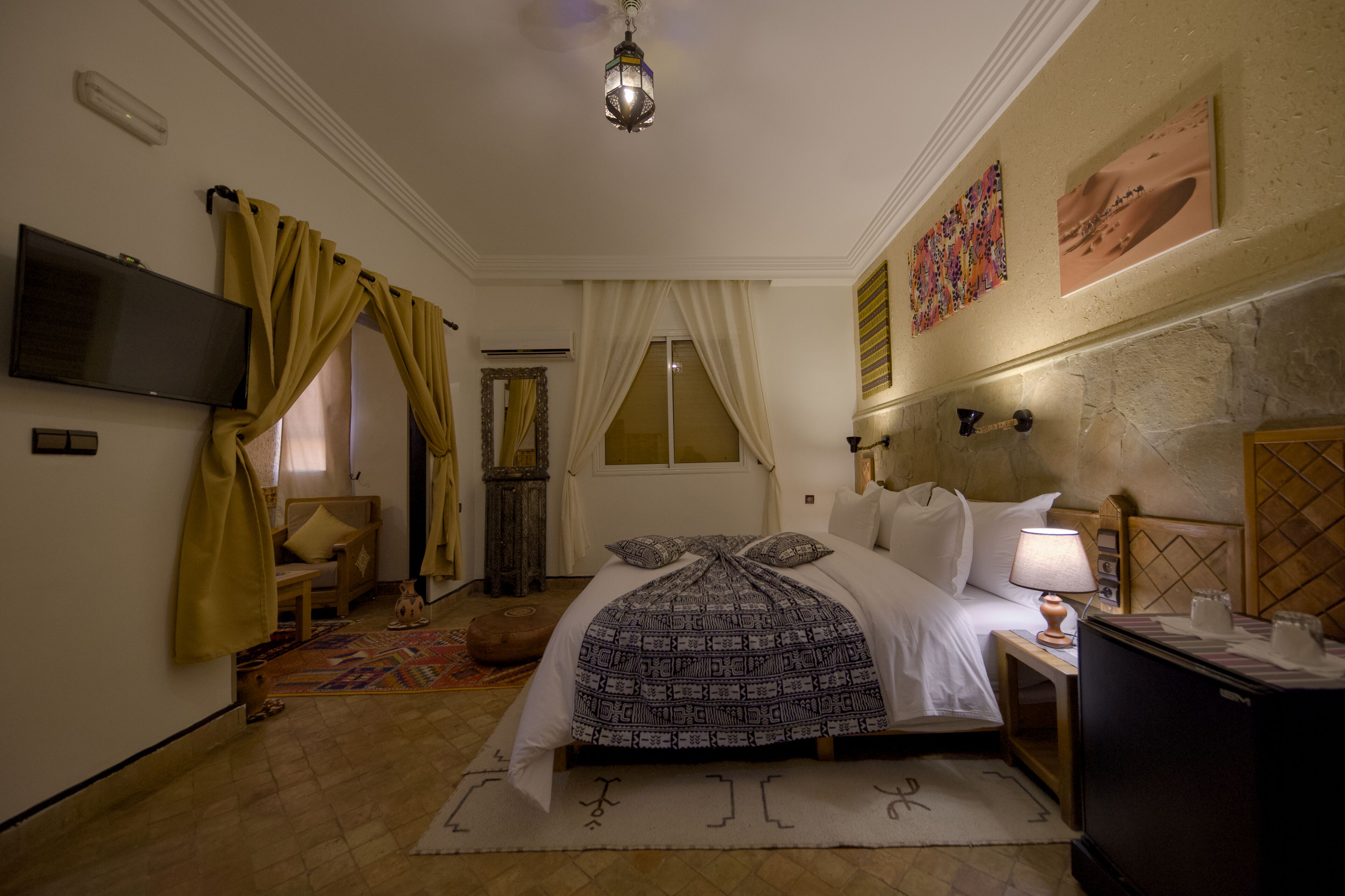 Una habitación de hotel con una cama, televisión, mesita de noche con lámpara y un adorno en la pared.
