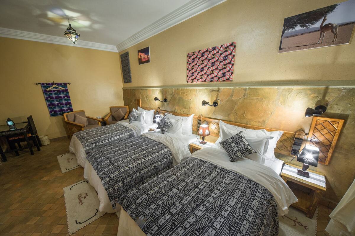 A hotel room with two beds, a desk, a chair, a lamp, and a wall-mounted picture.