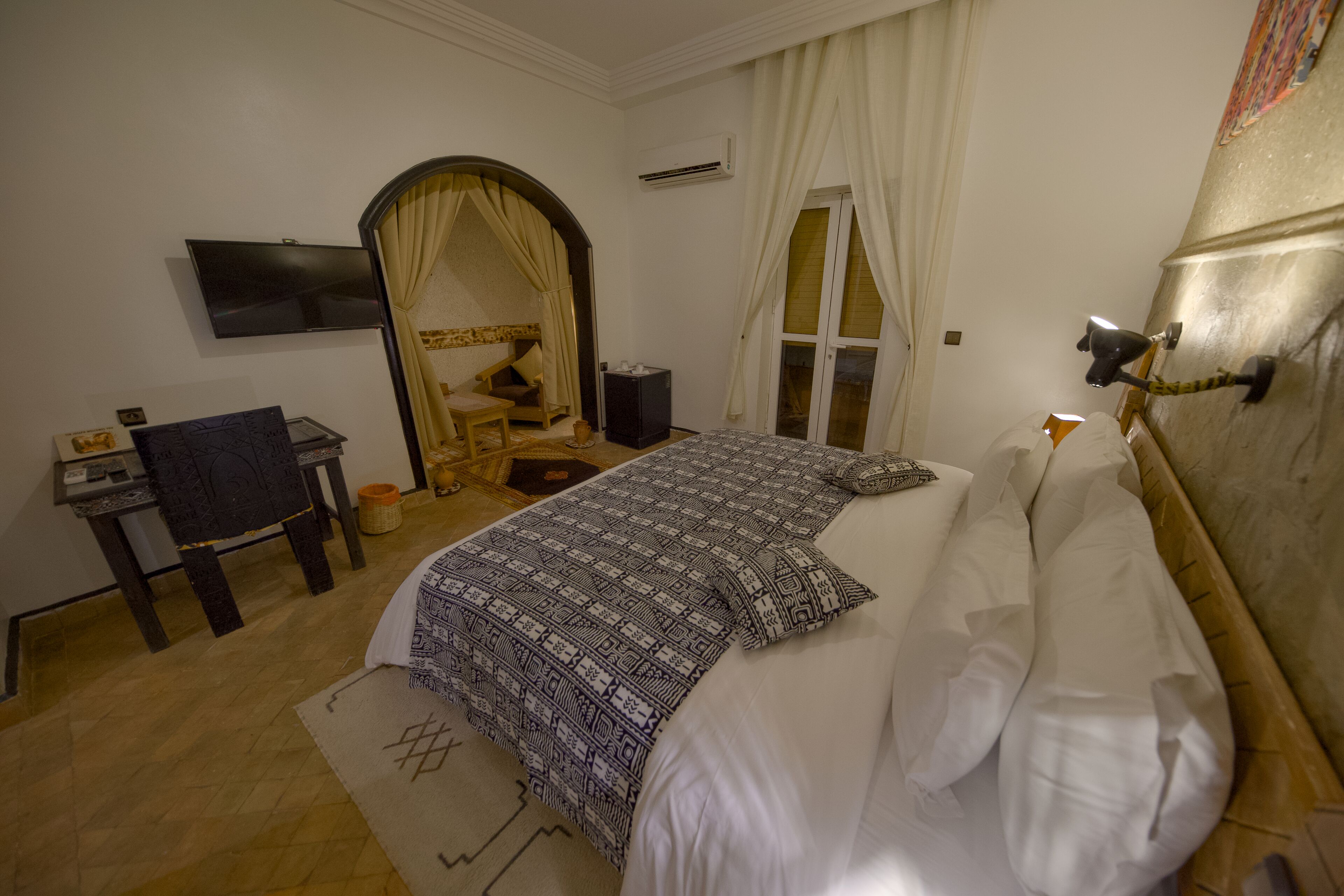 A hotel room with a bed, a desk, a chair, a TV, and a window with curtains.