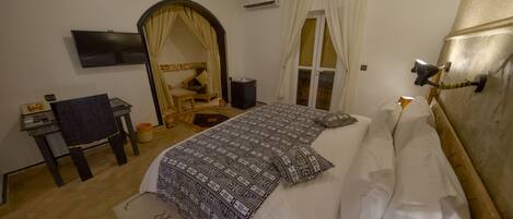 A hotel room with a bed, a desk, a chair, a TV, and a window with curtains.