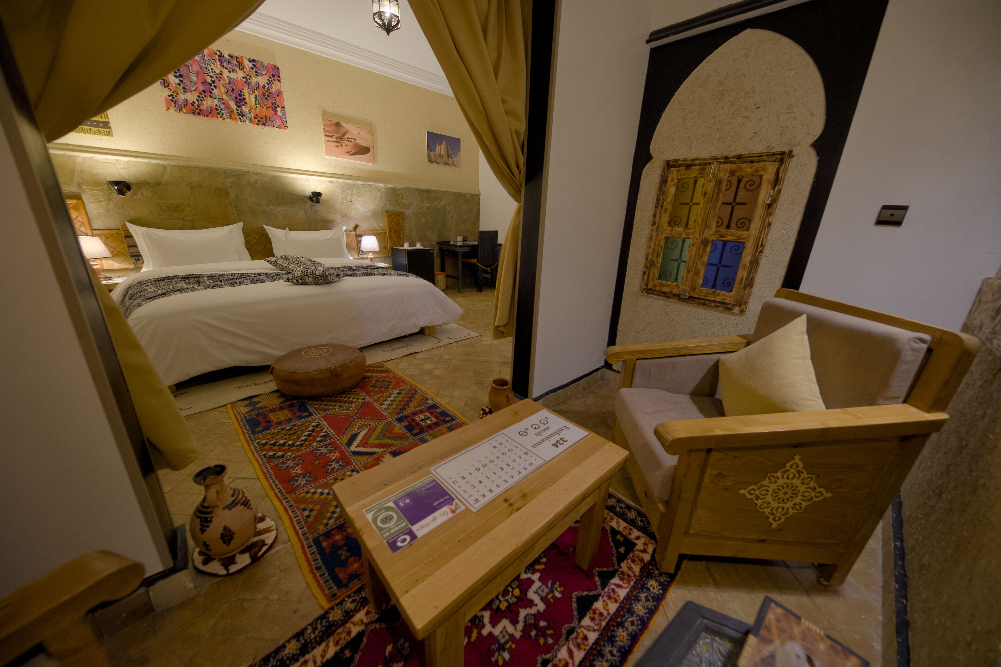 A hotel room with a bed, a wooden chair, a small table, and a decorative rug.