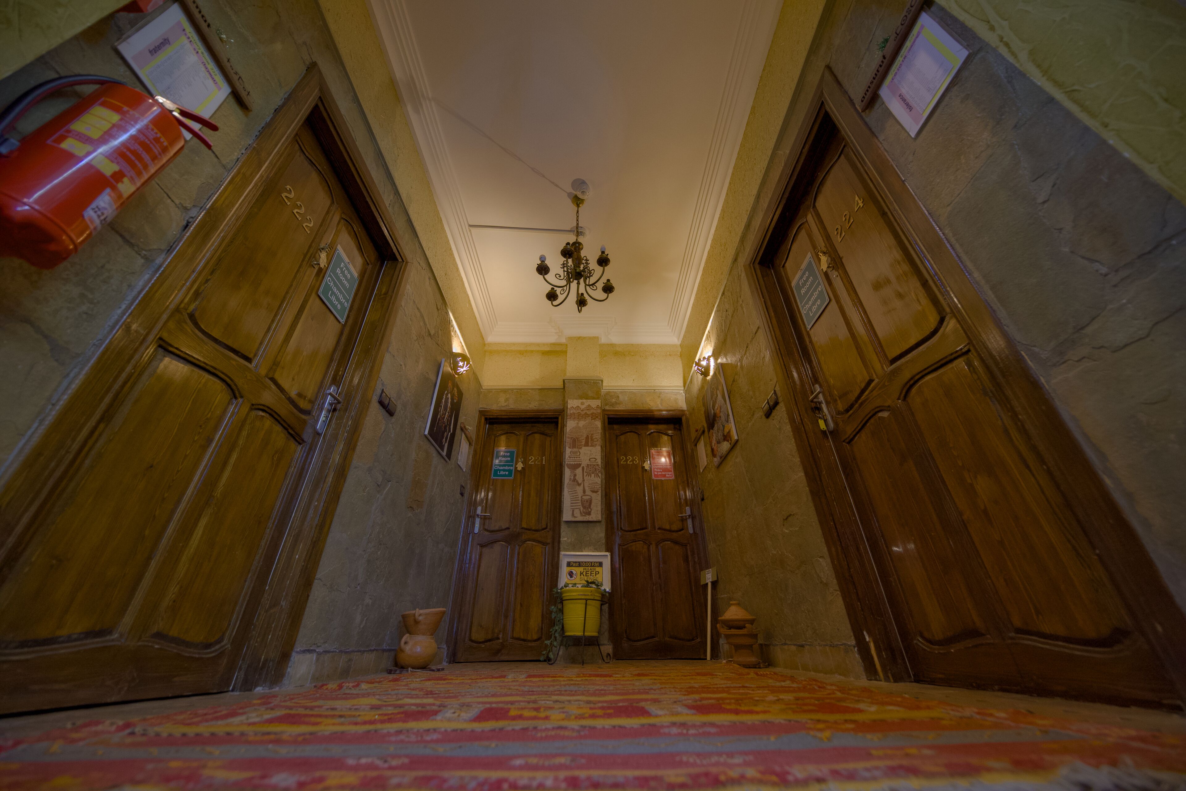 A hallway with wooden doors, a chandelier, and a patterned carpet.