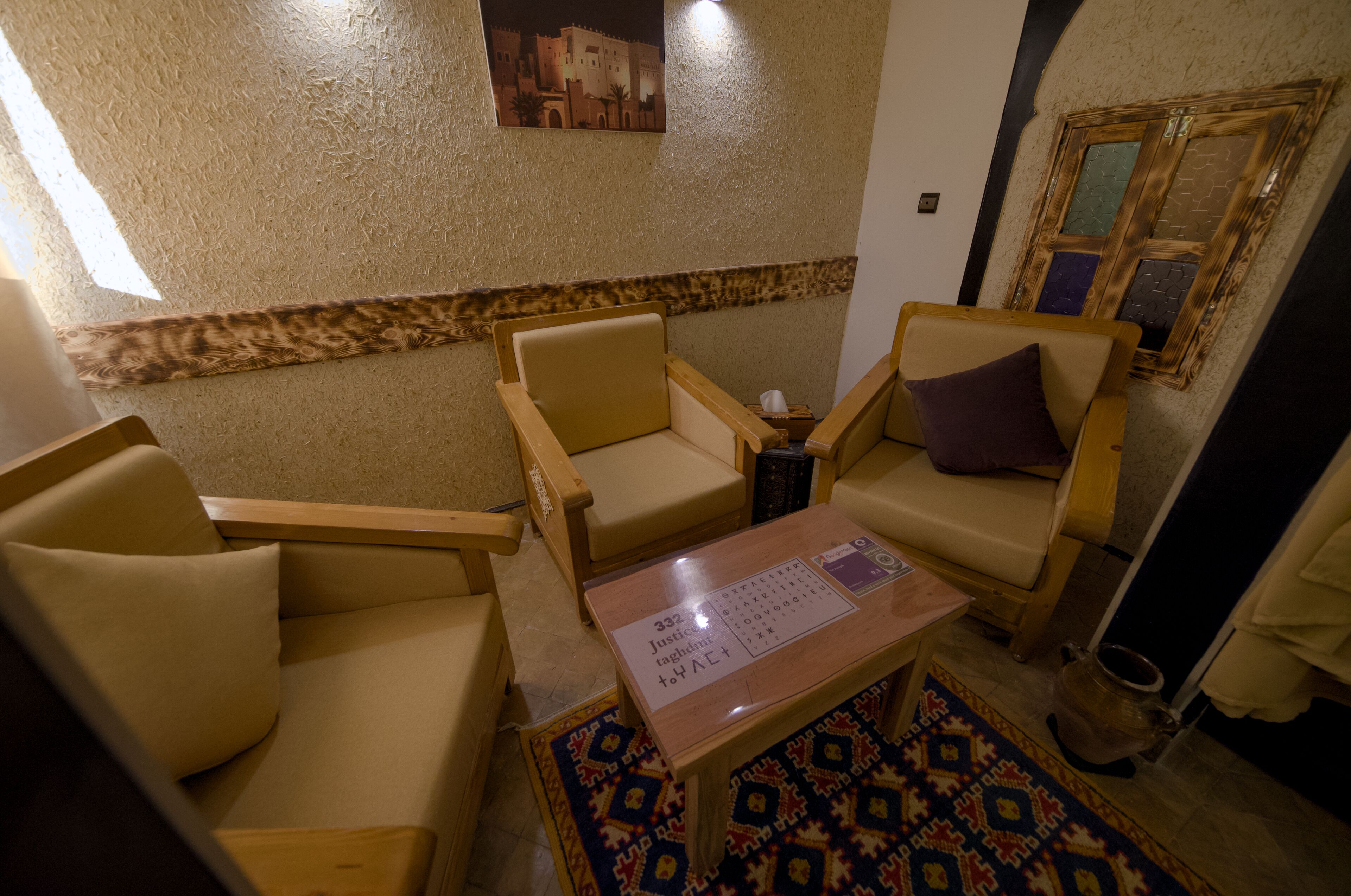 Una habitación con sofás color beige, una mesita con camino de mesa, una alfombra estampada y un cuadro colgado en la pared.