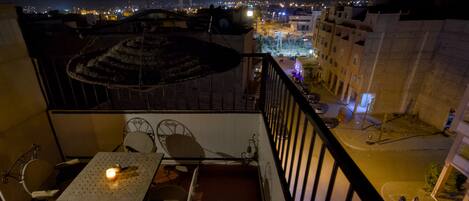 A balcony with a table and chairs, a patterned rug, and a view of the cityscape at night.