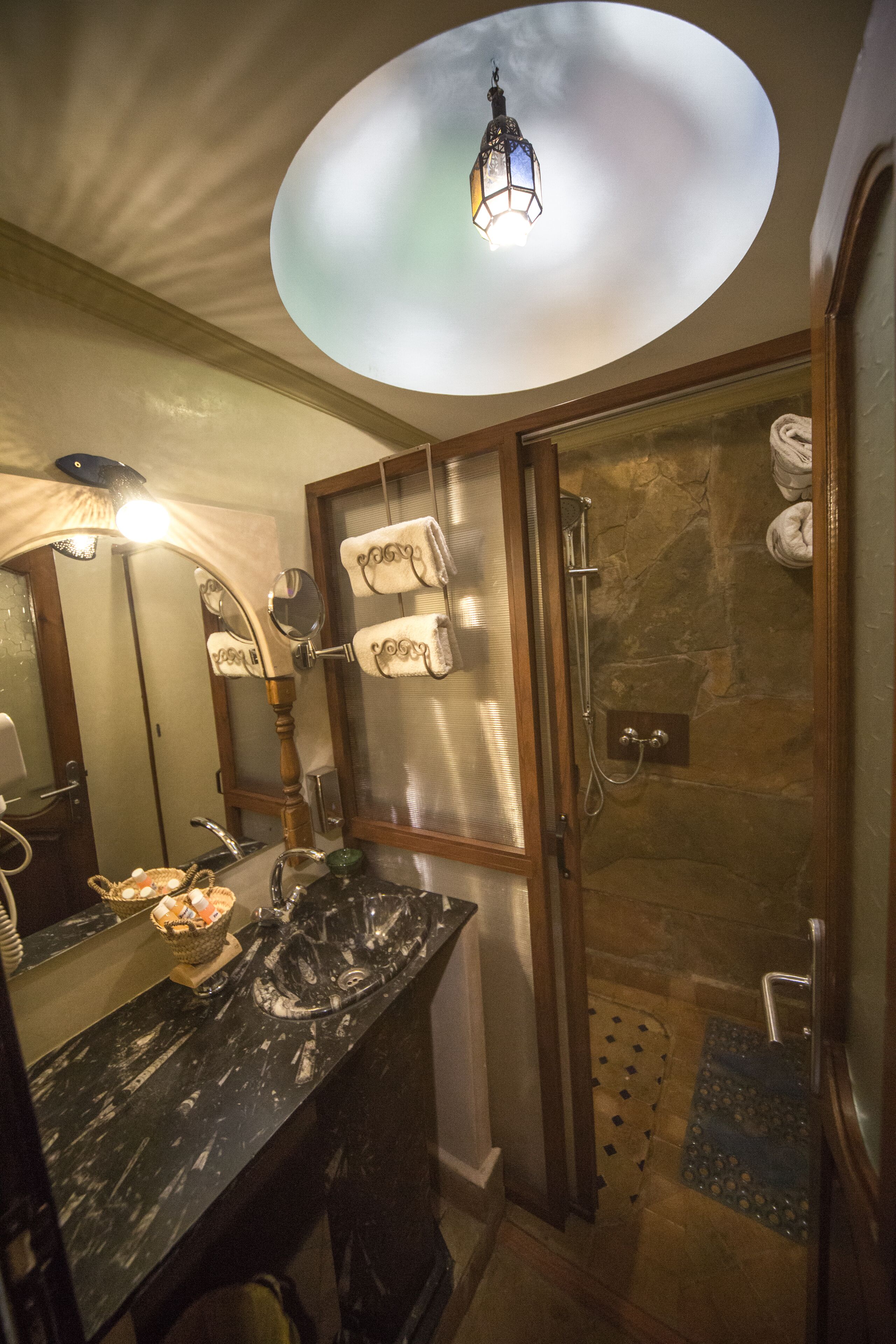 Une salle de bain avec un lavabo en marbre, une douche en verre et un luminaire encastré au plafond.