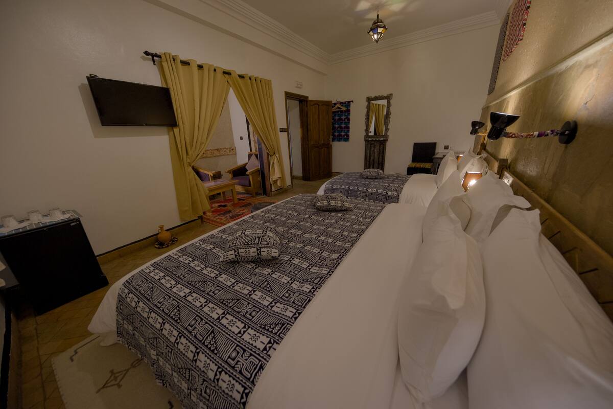 A hotel room with two beds, a television, a wardrobe, and a small table.