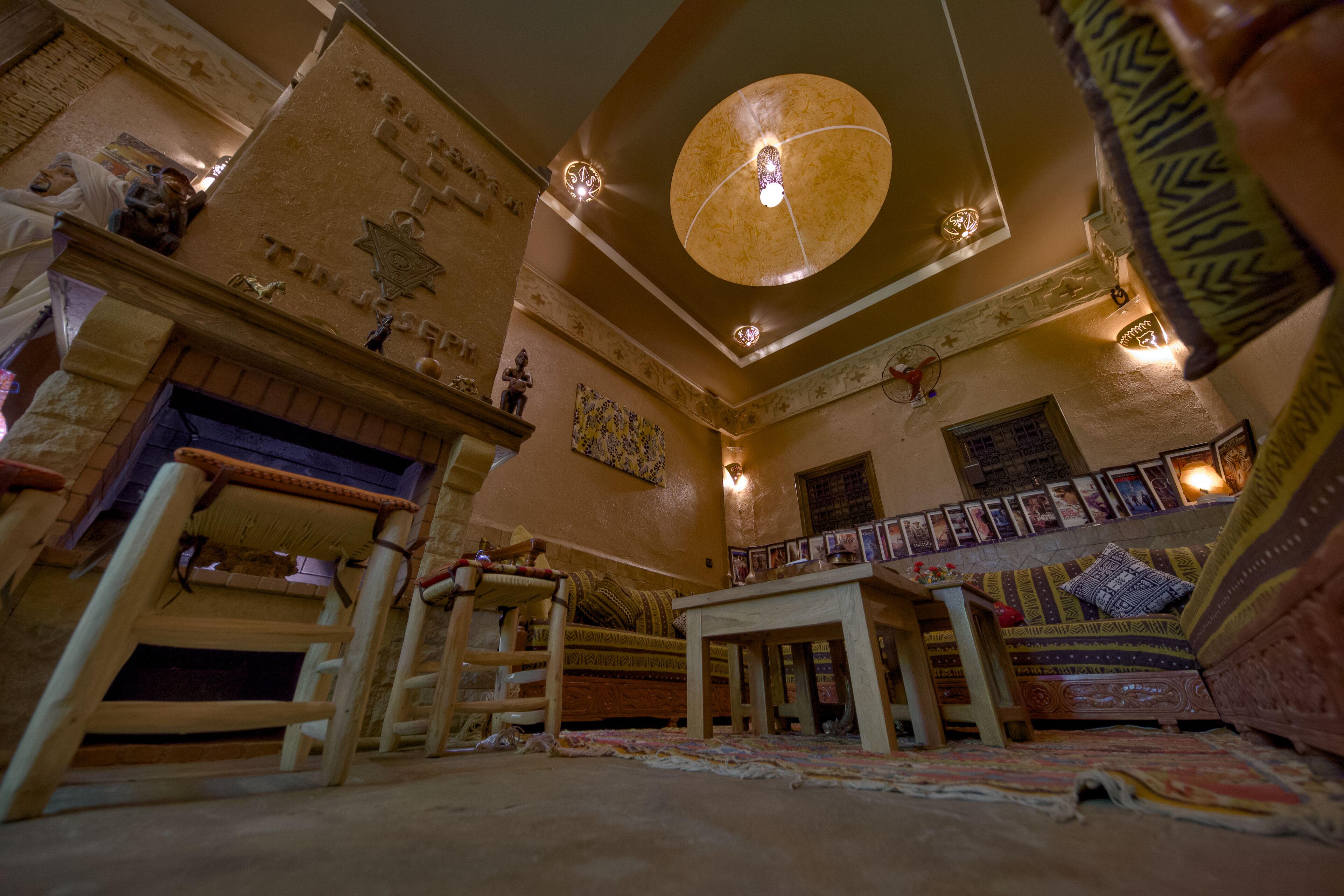 A cozy room with a high ceiling, a large chandelier, a wooden ladder, a bed with patterned bedding, and a small table.
