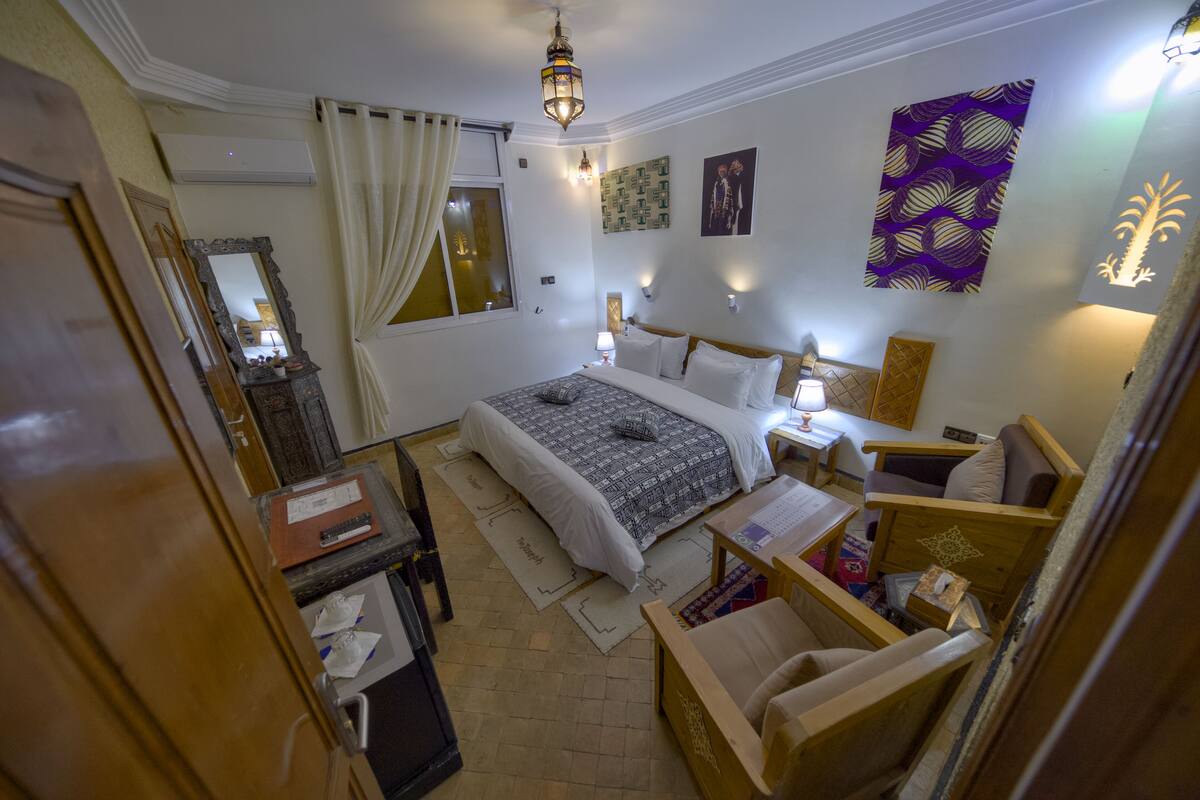 A bedroom with a bed, bedside table, lamp, and a mirror.