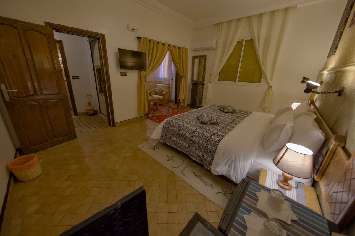 A bedroom with a bed, a bedside lamp, a television, and a window with curtains.