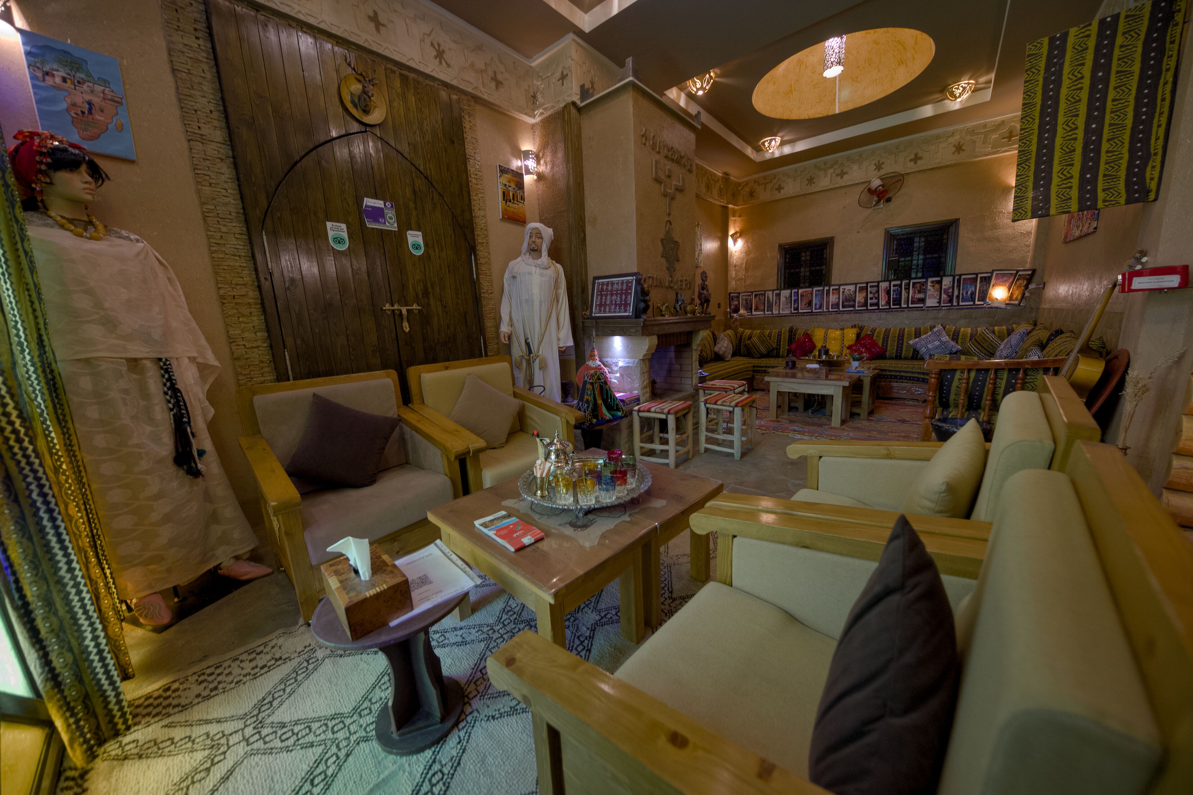 A cozy lounge area with wooden furniture, a fireplace, and a display of framed pictures on the wall.