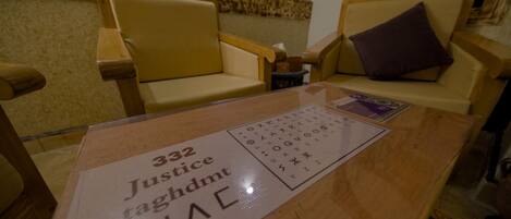 A room with a wooden table, two beige armchairs, and a small table with a sign reading "332 Justice taghdmt".