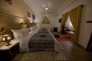 Una habitación de hotel con cama, mesita de noche, lámpara y ventana con cortinas.