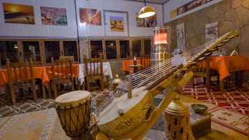 A room with tables covered in orange tablecloths, a large stringed instrument, and a drum.