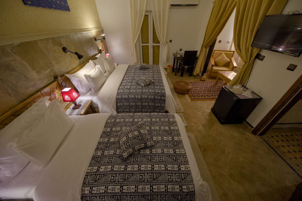 A hotel room with two beds, a TV, a desk, a chair, and a small table.
